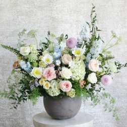 Large pastel arrangement of roses, hydrangeas and mixed blooms in a gray bowl vase on a pedestal table