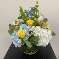Blue and white hydrangeas with yellow roses in a glass vase