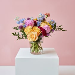 Mixed bouquet of yellow, pink, and blue flowers in a clear glass vase