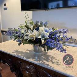 White lilies and blue flowers arranged in a silver vase