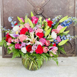 Mixed bouquet of pink, red, white, and blue flowers in a glass vase