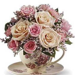 Pink and cream roses arranged in a floral teacup with saucer