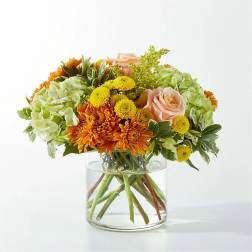 Bouquet of orange and yellow flowers with pale pink roses in a clear glass vase