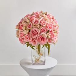 Pink rose bouquet in a clear glass vase on a white pedestal