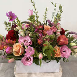 Large mixed bouquet in a white rectangular vase with pink, peach, and red blooms.
