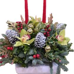 Holiday floral centerpiece with red candles, pinecones, and orchids in a white container