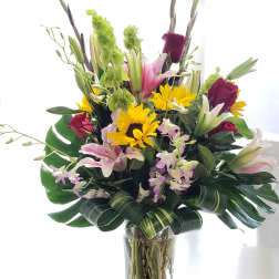 Tall mixed bouquet in a clear glass vase with lilies, roses, and sunflowers