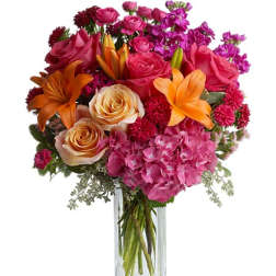 Mixed bouquet of pink roses, orange lilies, and hydrangeas in a glass vase