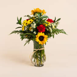Bouquet of sunflowers, daisies, and red carnations in a glass vase