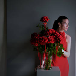 Red roses in a glass vase beside a woman in a red dress