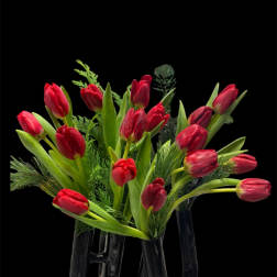 Red tulips arranged in a clear glass vase with greenery