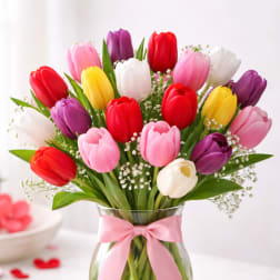Colorful tulips in a glass vase with a pink ribbon