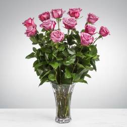 Tall arrangement of lavender-pink roses with abundant foliage in a clear glass vase