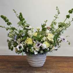 Low floral arrangement in a textured white pot with pale roses and white blooms
