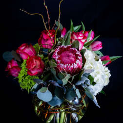 Bouquet of pink roses, a protea, and white hydrangeas in a glass vase