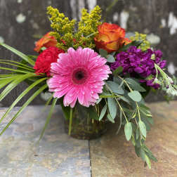 Mixed bouquet with pink gerbera, orange roses, and purple flowers in a glass vase