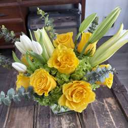 Yellow roses and white tulips arranged in a glass vase