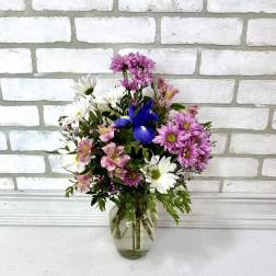 Mixed bouquet of pink, white, and blue flowers in a clear glass vase