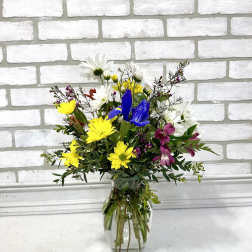 Mixed bouquet of yellow, white, blue, and purple flowers in a clear glass vase