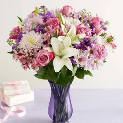Pink and white mixed flower bouquet in a purple glass vase