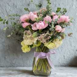 Pink and cream flowers in a glass vase with a lavender ribbon