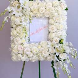 White floral wreath on an easel with roses and lilies