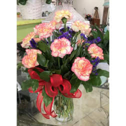 Bouquet of pink and yellow carnations with purple filler in a clear vase