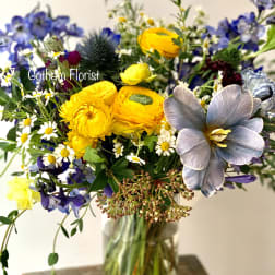 Mixed bouquet in a clear glass vase with yellow, blue, and white flowers