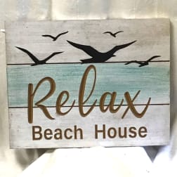 Wooden sign reading Relax Beach House with bird silhouettes
