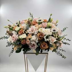Large pastel floral arrangement in a white container on a gold stand