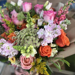 Mixed bouquet of pink, orange, and lavender flowers wrapped in brown paper