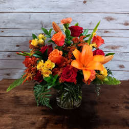 Mixed bouquet of orange, red, and yellow flowers in a glass vase