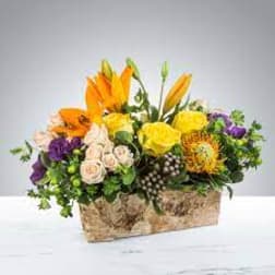 Mixed bouquet in a rectangular basket with orange, yellow, purple, and cream flowers