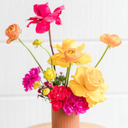 Bright mixed bouquet in a ribbed vase with pink, yellow, and orange blooms