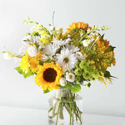 Bouquet of sunflowers, white daisies, and yellow flowers in a clear glass vase