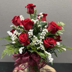 Red roses arranged in a glass vase with white filler flowers and a burgundy ribbon