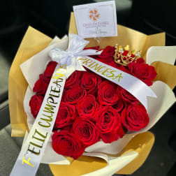 Bouquet of red roses wrapped in gold and white paper with a ribbon and crown topper