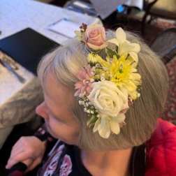 Floral hairpiece with pink, white, and yellow flowers worn in gray hair