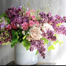 Pink roses and purple lilacs arranged in a white vase