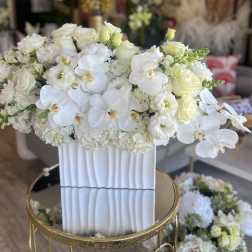 White floral arrangement in a tall ribbed vase with orchids and roses