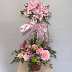 Pink floral arrangement with a butterfly topper and ribbon in a vase