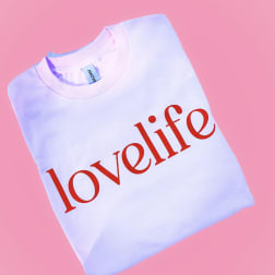 Folded white sweatshirt with red "lovelife" text on a pink background