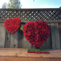 Two red heart-shaped floral arrangements on stands, one made of roses