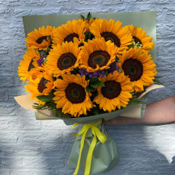 Bouquet of bright yellow sunflowers wrapped in green paper with a yellow ribbon