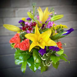Bright mixed bouquet with yellow lilies, coral roses, and purple accents in a vase