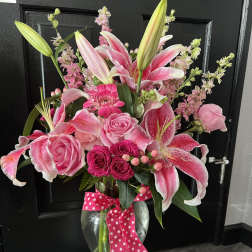 Pink lilies and roses arranged in a glass vase with a polka-dot ribbon