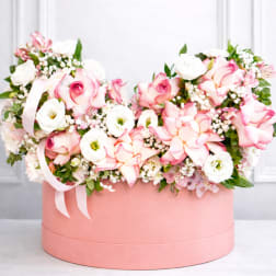 Pink and white roses arranged in a round pink box with ribbon