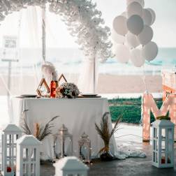 Beachside wedding table with white floral arch, balloons, and lanterns