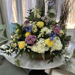 Basket arrangement of yellow roses, white hydrangeas, and purple flowers