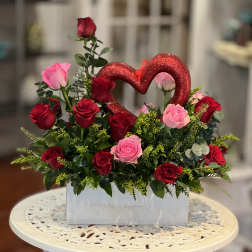 Red and pink roses arranged in a white box with a glitter heart pick